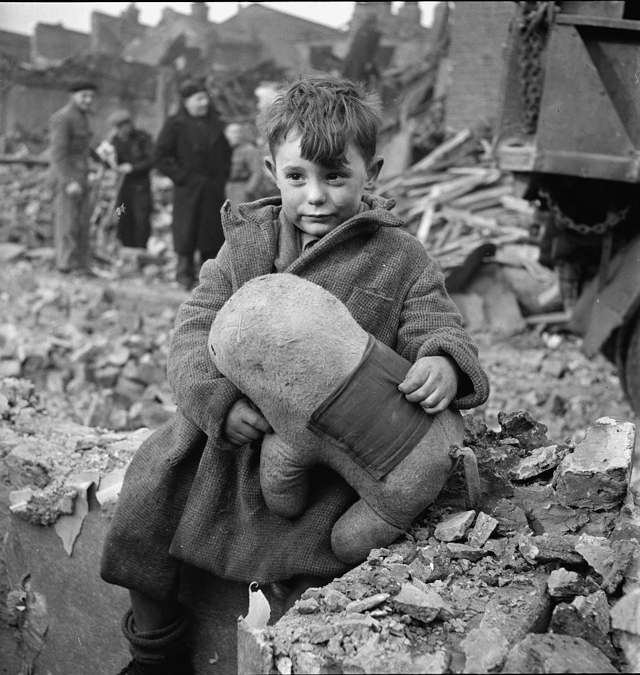 Abandoned boy holding a stuffed toy animal amid ruins following German aerial bombing of London, England, United Kingdom, 1940