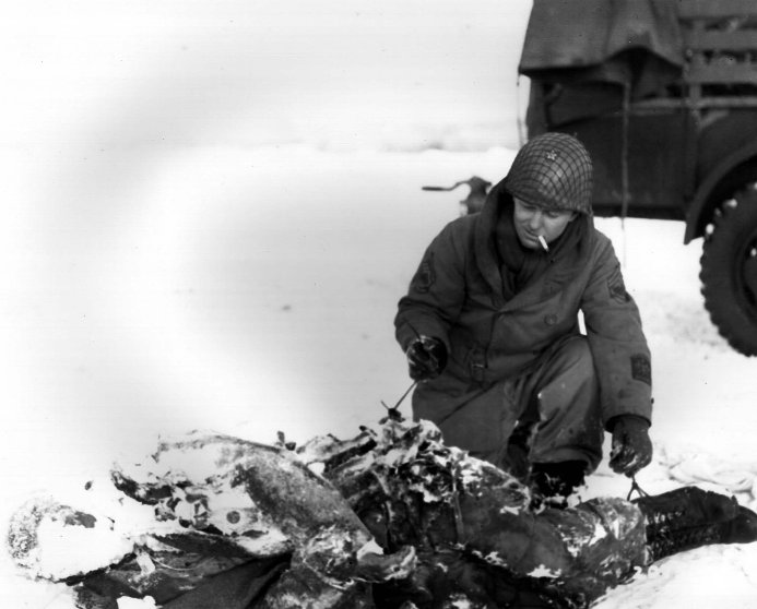 US Army Signal Corps Technical Sergeant Harry A. Downard looking at a killed paratrooper of US 101st Airborne Division, near Bastogne, Belgium, 12 Jan 1945