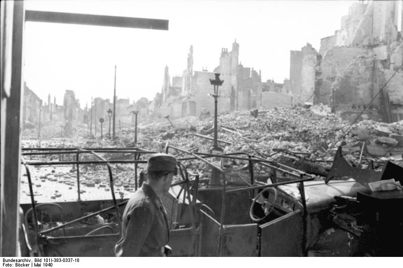 A German soldier looking at destroyed car and buildings, Calais, France, May 1940