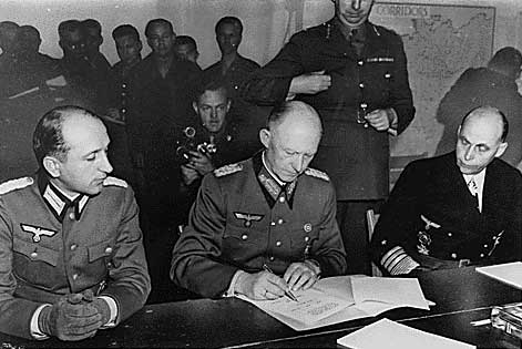 Jodl signing surrender documents at Eisenhower's headquarters, flanked by Major Wilhelm Oxenius and Admiral Hans-Georg von Friedeburg, Reims, France, 7 May 1945, photo 1 of 4
