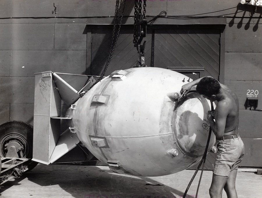 Technician spraying 'Fat Man' bomb with plastic paint in front of Assembly Building Number 2, Tinian, Mariana Islands, Aug 1945, photo 1 of 4
