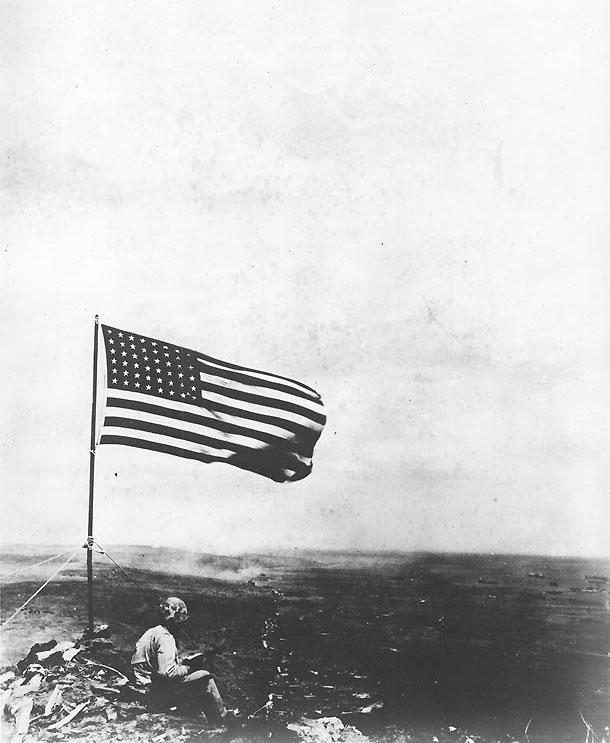 An American Marine sat beneath the American flag atop Mount Suribachi, Iwo Jima, Japan, 23 Feb 1945
