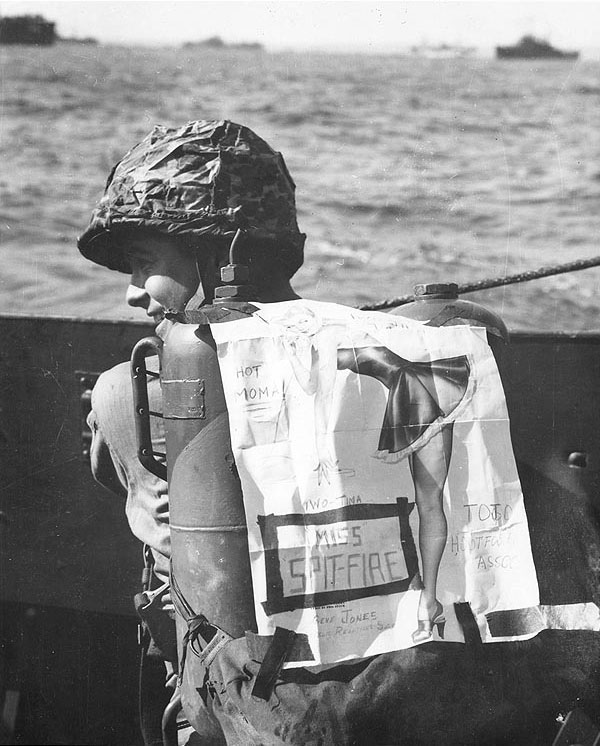 US Marine Private Kenneth R. Hager with his pin-up decorated flamethrower pack, off Iwo Jima, Feb 1945