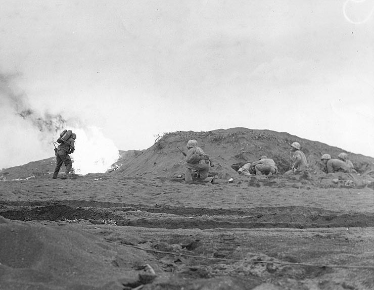 US Fifth Marine Division riflemen waited while a fellow Marine burned out a Japanese-held cave with flame thrower, Iwo Jima, 26 Feb 1945