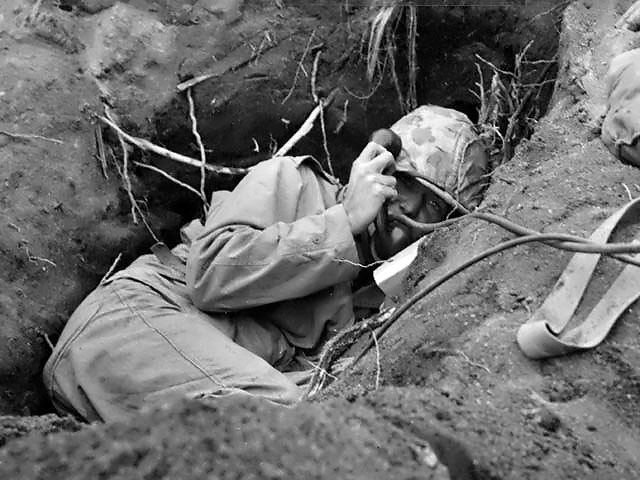 Burrowed in his shallow foxhole at the edge of Motoyama airstrip on Iwo Jima, an US Marine communicator called for artillery support, Feb 1945