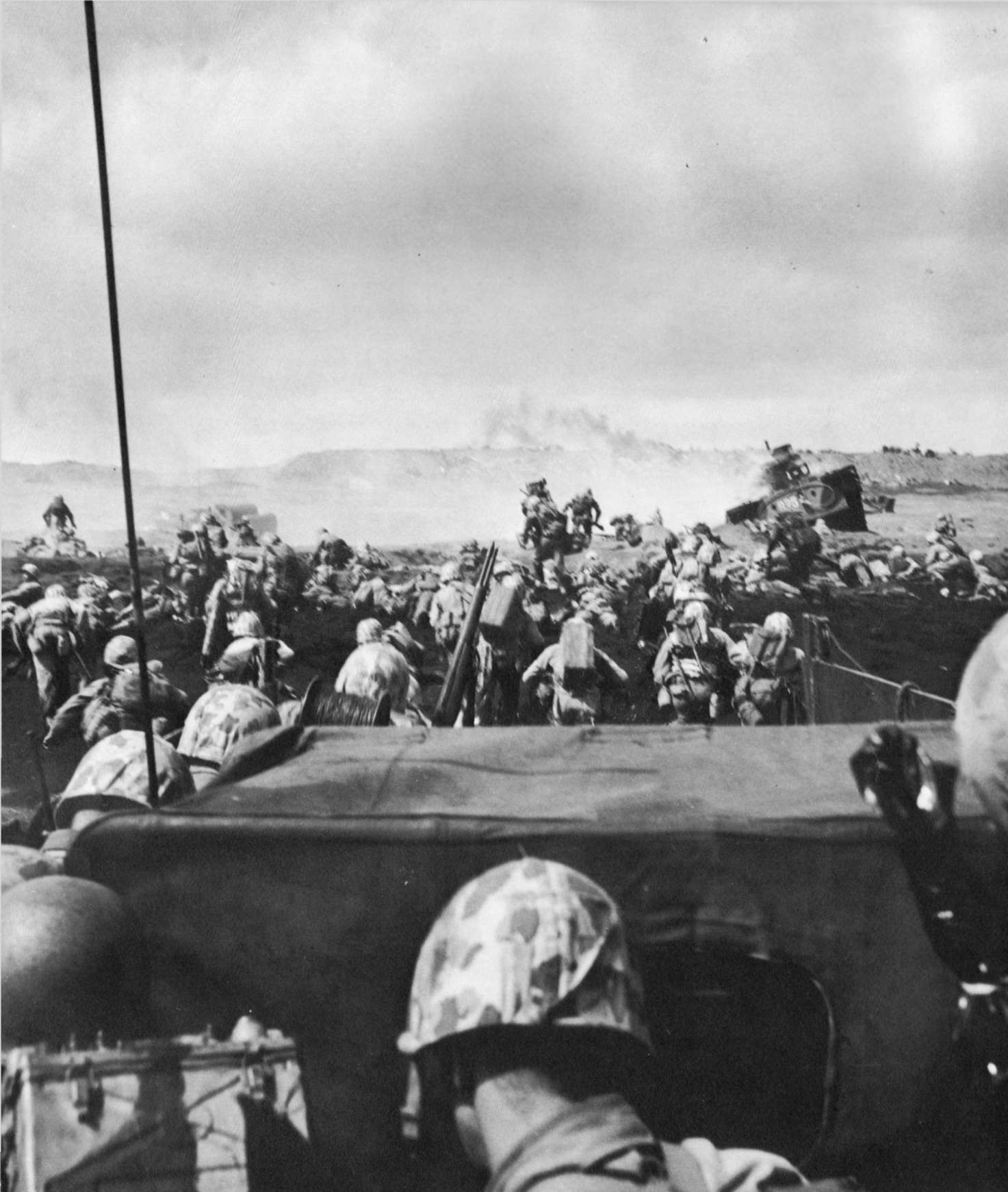 Men of the US 4th Marines rushing out of their landing craft for Iwo Jima landing beach, 19 Feb 1945, photo 1 of 2; note LVT burning in right center