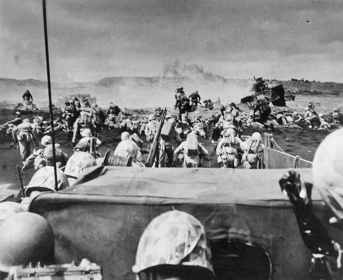 Men of the US 4th Marines rushing out of their landing craft for Iwo Jima landing beach, 19 Feb 1945, photo 2 of 2; note LVT burning in right center