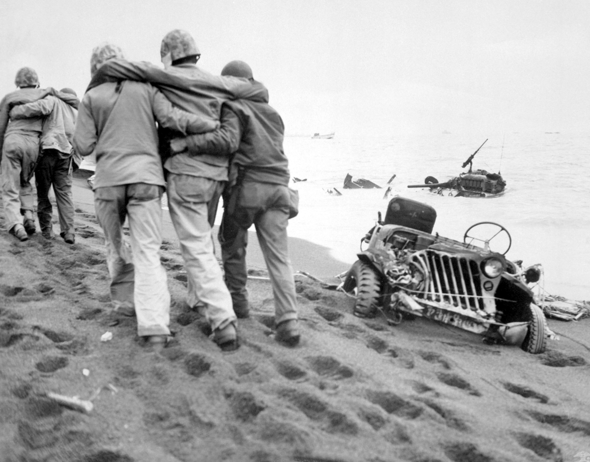Navy corpsmen helped a wounded Marine to reach an aid station, Iwo Jima, Feb-Mar 1945. Note crushed Jeep and submerged M4 Sherman tank.