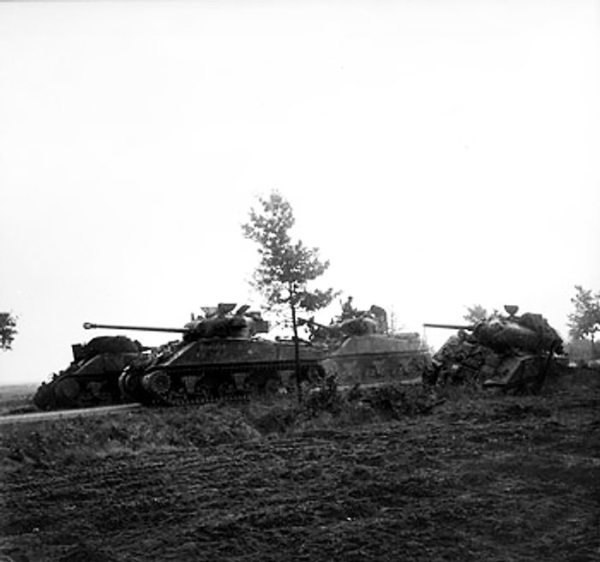 A Sherman Firefly tank of the UK Irish Guards Group advancing past Sherman tanks knocked out in previous actions, the Netherlands, 17 Sep 1944