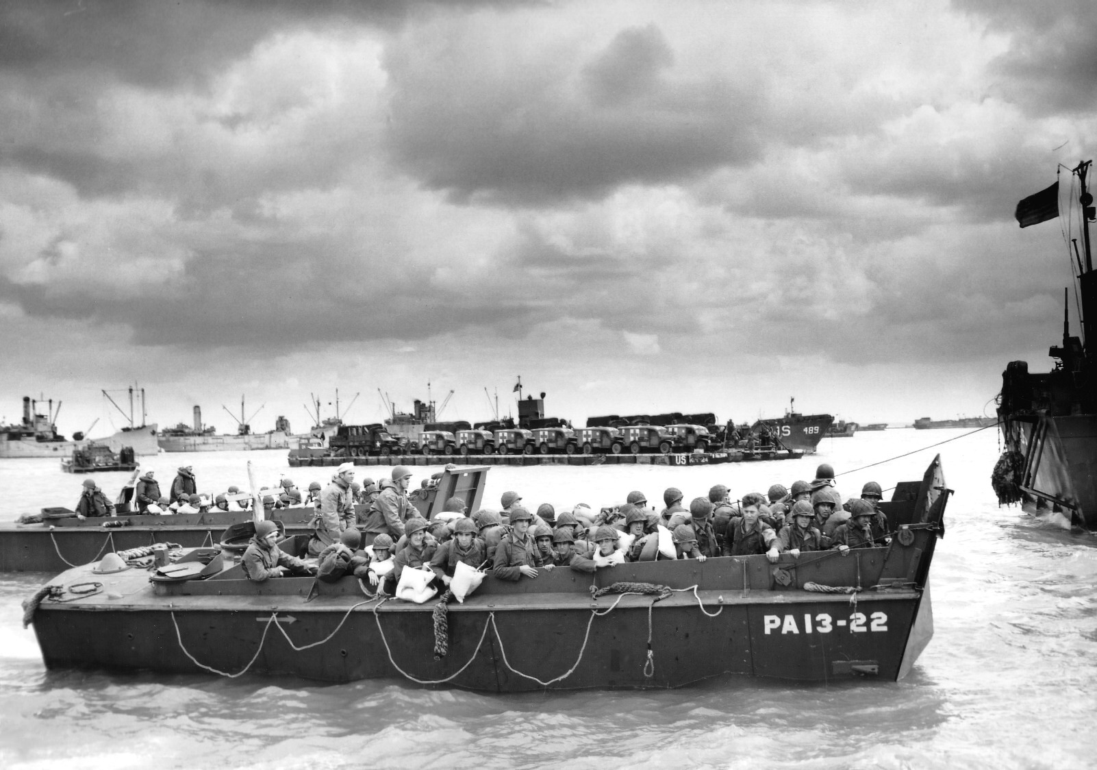 In a port in England, a loaded LCVP Landing Craft from the Attack Transport USS Joseph T. Dickman brought troops to the ship for the crossing to Normandy, June 1944. Note Rhino barge loaded with WC54 Ambulances