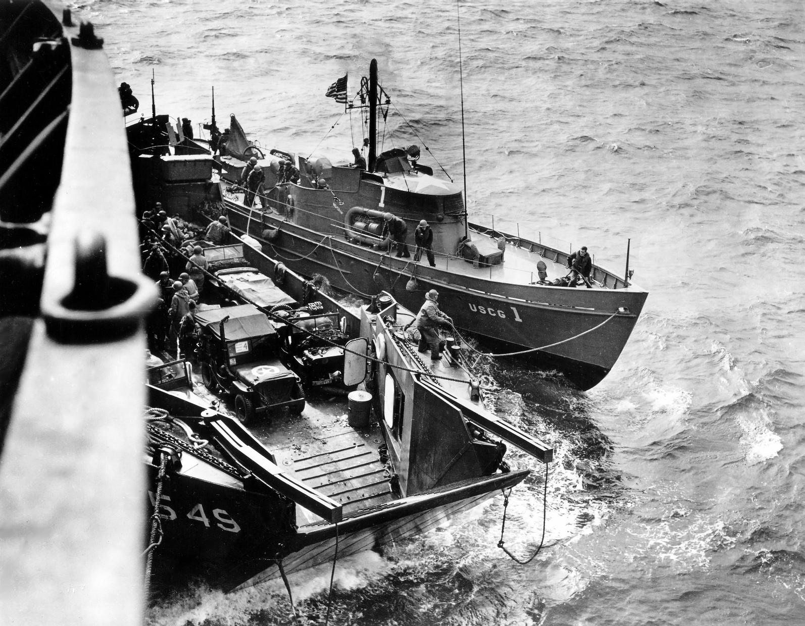 A LCT and an US Coast Guard-manned boat operating off Normandy, France, Jun 1944; note jeep vehicles onboard the LCT