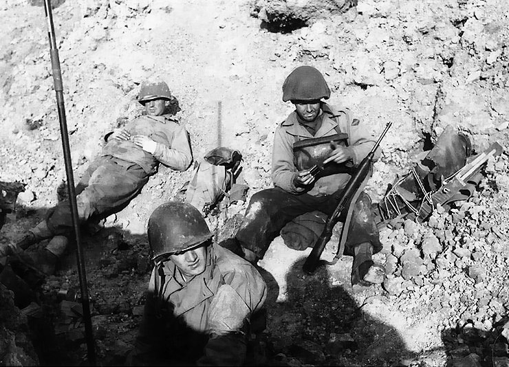 US Army Rangers resting near Pointe du Hoc, Normandy, France, inland from Omaha Beach, 6 Jun 1944; note soldier using finger to push cartriges into magazine of his M1 Carbine