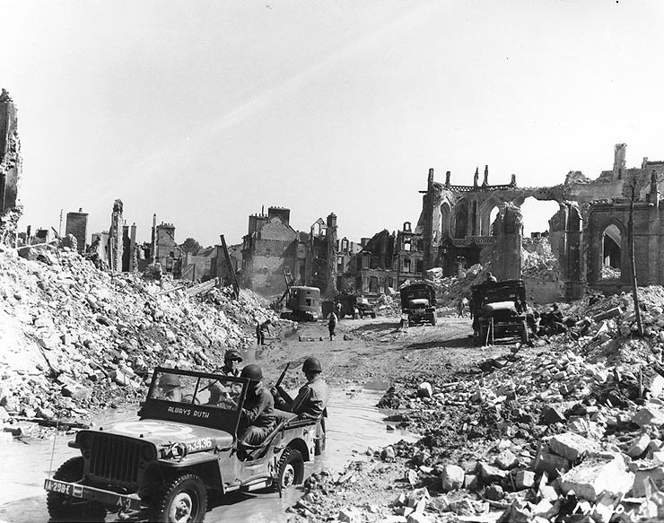 View of the town of Valognes, devastated by Allied bombing during the Cherbourg battle, 24 Jun 1944; note jeep 'Always Ruth' in foreground