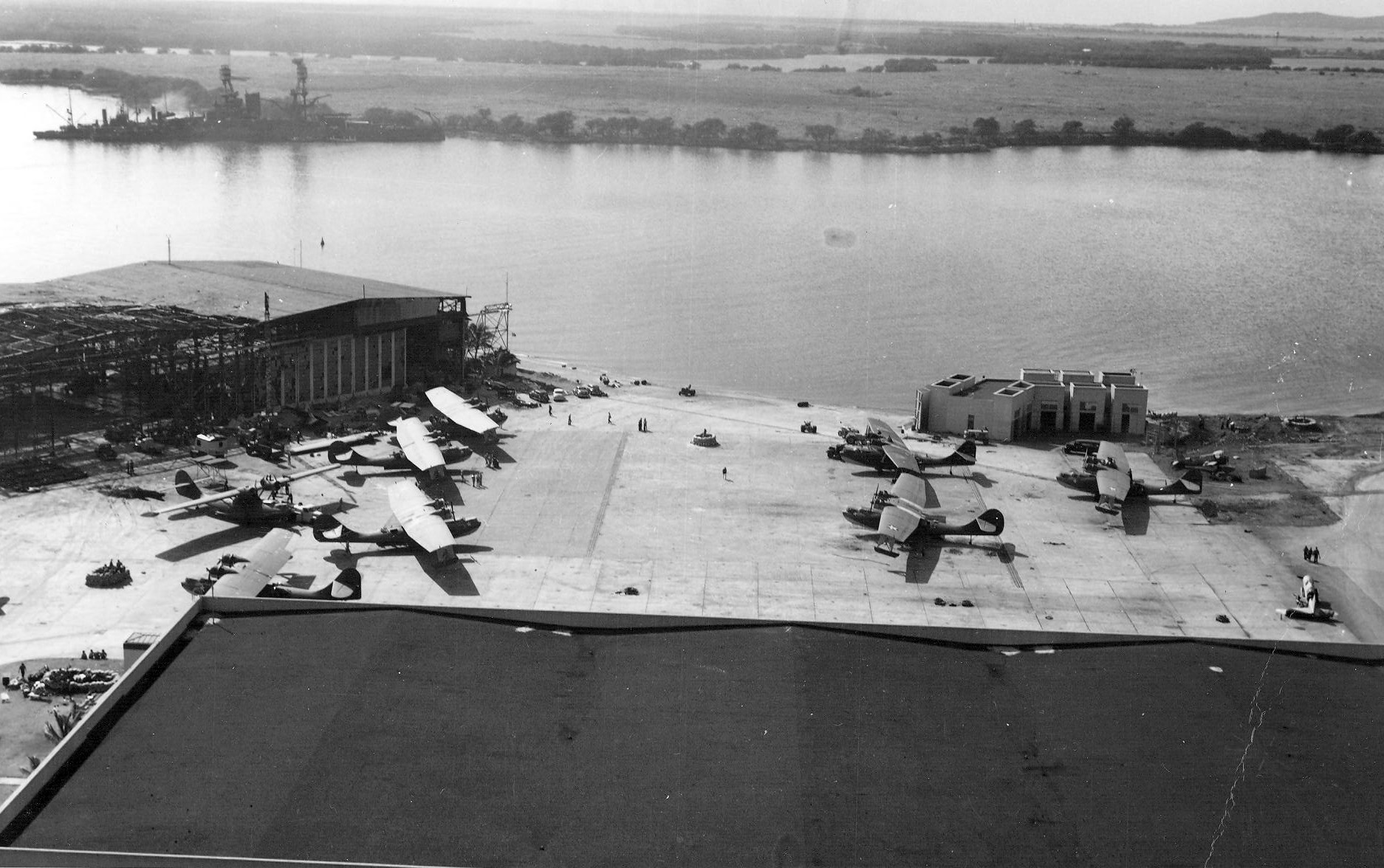View of Naval Air Station Ford Island, Oahu, US Territory of Hawaii, 8 Dec 1941 from the Ford Island water tower; note PBY aircraft on the ramp and USS Nevada after her move from Hospital Point to the Waipio Peninsula