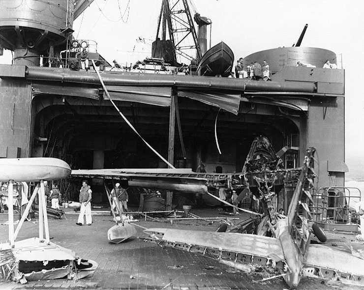 Damage to hangar doors of seaplane tender USS Curtiss by Japanese 250kg bomb during Pearl Harbor attack, 7 Dec 1941, photo 1 of 2; note wreckage of OS2U-2 floatplane in foreground