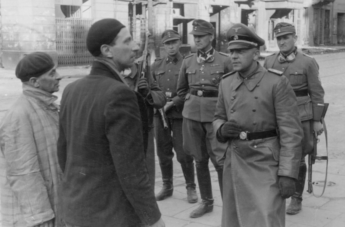 German officer (possibly SS General Maximilian von Herff) questioning Jews in Warsaw, Poland, 14-15 May 1943; note Jürgen Stroop (with goggles) and Karl Kaleske (or Erich Steidtmann; first from right) in background
