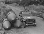 A member of the 2107th Ordinance-Ammo Battalion inspecting a store of 4000-pound bombs, some under camouflage netting, along the roadside at the Sharnbrook Ordinance  Depot, Bedfordshire, England, UK.  July 1943