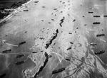 13 Liberty Ships deliberately scuttled to form a breakwater for invasion vessels landing on the Normandy beachhead lie in line off the beach shielding the ships in shore.