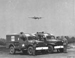 Medical staff and their WC-54 ambulances waiting for returning B-17 bombers, probably at RAF Ridgewell, Essex, England, United Kingdom, 1944-45. Note the flare shot from the B-17 indicating wounded personnel on board