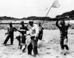 Worth Buttram, Leonard Busby, Edwin Fogolman, Lieutenant Samuel Raymond (with white flag), and Edward Patot escorting a Japanese prisoner, Kerama Retto, Japan, Aug-Sep 1945