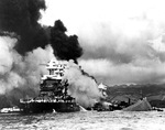 A bow-on view of the comparatively lightly damaged battleship USS Maryland with the burning USS West Virginia behind her and the capsized USS Oklahoma beside her, Pearl Harbor, US Territory of Hawaii, 7 Dec 1941