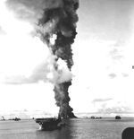 A column of smoke 500 feet wide rising from the burning fleet oiler USS Mississinewa after being struck by the first Japanese Kaiten deployed, Ulithi Atoll, 30 Nov 1944. Light carrier USS Langley is in the foreground.