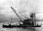 Seaplane derrick YSD-19 “Mary Ann” crossing the harbor with the wreckage of Japanese Aichi D3A “Val” dive bomber that crashed in water during Pearl Harbor attack, Dec 1941.