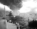 A view down Pearl Harbor’s Battleship Row about an hour after the Japanese air attack began, 0850, 7 Dec 1941. Note battleship USS California listing in the foreground and the capsized Oklahoma beyond.