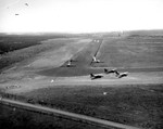 Aerial view of CG-4A gliders landing in groups of three at a glider training airstrip in Texas, 1943. One C-47 Skytrain tow plane is visible in the upper left.