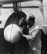 Member of the 894th Chemical Company inserting the fuse into a tank of napalm slung under the wing of a P-38J Lightning of the 8th Fighter Group at Elmore Airfield, Mindoro, Philippines, Apr 1945.