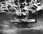 USS Enterprise berthed on the north side of Ford Island in Pearl Harbor, Hawaii, 12 Jul 1942. Note the submarine nets, the F4F Wildcat on an aircraft barge alongside, and the camouflaged buildings on the island.