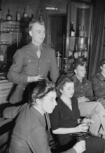 WAAF Aircraftwoman 2nd Class Patricia Graham, US Army Corporal H. Bielski, WAAF Aircraftwoman 2nd Class Maclean, and US Army Lieutenant Peyton Mathias listening to a radio broadcast at the Over-Seas Club of St James