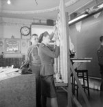 British WAAF member and an American non-commissioned officer recording the arrival of an American aircraft in the operations room of US Air Transport Command at Prestwick Airport, Scotland, United Kingdom, 1944