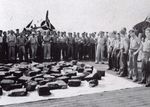 Crew and aviators of USS Bogue looking at bales of raw rubber recovered from the debris field after sinking Japanese submarine I-52 in the mid-Atlantic, 24 Jun 1944. Note the FM-2 Wildcat.