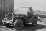 Royal Canadian Air Force pilot in a Jeep at the Meaford Armoured Fighting Vehicle Range, Meaford, Ontario, Canada, 1944. Note the visors over the Jeep’s headlights and the universal carrier in the background.