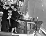Josephine Doolittle, wife of James Doolittle, breaking a bottle of champagne at the launching ceremony of carrier Shangri-La, Norfolk Navy Yard, Portsmouth, Virginia, United States, 24 Feb 1944, photo 1 of 2; note yard commandant Rear Admiral Felix Gygax holding a microphone near the bottle