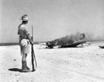 Australian soldier observing the burning wreck of Ju 87B Stuka dive bomber, near Tobruk, Libya, 1941