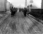 Men of US 28th Infantry Division marching down a street in Bastogne, Belgium, 20 Dec 1944