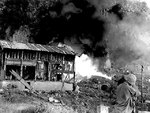 US Marine with flamethrower attacking a Japanese position, northern Saipan, Mariana Islands, 12 Jul 1944; note the scorched building on left
