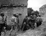 A platoon of African-American troops of the US Army moving along a farm house as they prepared to eliminate a German sniper up ahead, near Vierville-sur-Mer, France, 10 Jun 1944