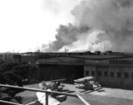 View of Pearl Harbor smoke columns from Naval Air Station Ford Island, US Territory of Hawaii, 7 Dec 1941; note J2F aircraft, RD-3 aircraft, Hangar 37 building, USS Pennsylvania, and USS Nevada
