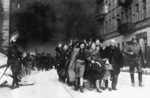 Yehudit Neyer (dark-haired woman), madam Neyer (center), Avraham Neyer (next to child), and the rest of the Neyer family leading a column of Jews being marched out of the Warsaw ghetto gate for deportation, Warsaw, Poland, Apr-May 1943, photo 1 of 2