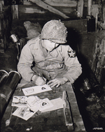Pvt Walter Prsybyla of B Btry, 37th Field Artillery Regt, US 2nd Inf Div writing Christmas cards for friends and family from an artillery ammunition storehouse, Heckhalenfeld, Germany, 30 Nov 1944