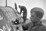 A Soviet mechanic working on a fighter aircraft while a crew member stenciled a star on the fuselage, Russia, 1 Jul 1942