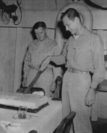Lieutenant F. B. Underman (cutting cake) and Commander E. W. Davis celebrating the 5,000th landing aboard USS Anzio, 16 Apr 1945