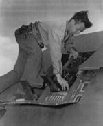 Aviation Ordnanceman 1st Class Billy Simms inspecting the wing guns of a fighter aircraft aboard USS Anzio, 18 Apr 1945