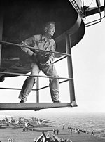 LtCdr Edward Steichen with his camera on an island catwalk above the flight deck of the USS Lexington (Essex-class), Nov 1943, probably off Hawaii. Note F6F Hellcats on the flight deck.