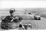 A German soldier with headphones and binoculars at an open hatch of a tank, Southern Russia, mid-1942; note SdKfz. 251 halftrack vehicles and Panzer II tanks in background