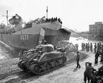 LST-77 off-loading M4 Sherman tanks at Anzio, Italy, May 1944; note the small barge capsized in the background and LCVP on the LST