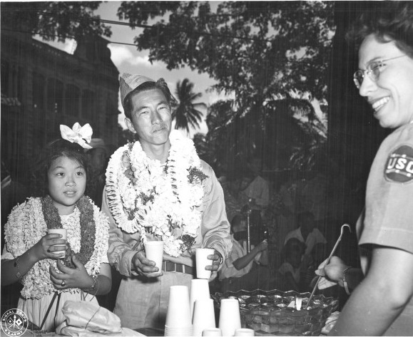 Returning Japanese-American soldier of US 442nd Regimental Combat Team visiting the refreshments table set up by the USO at the Iolani Palace grounds, Honolulu, US Territory of Hawaii, 9 Aug 1946